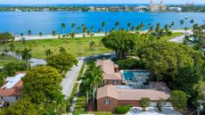 aerial view of large home with palm trees and large grass area by the ocean