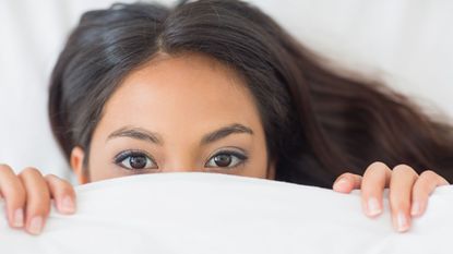 Young girl peeking from underneath a duvet