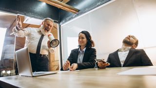 A stock photo showing a person acting as an angry boss with a megaphone, screaming at employees in an office, looking scared and annoyed (Credit: master1305 via Getty Images)