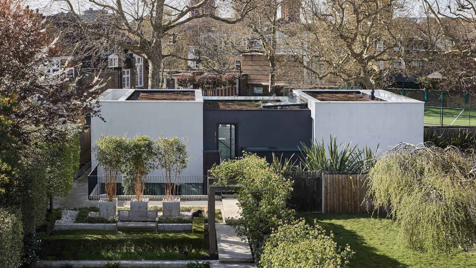 A renovation of a property including two new builds with white cladding, connected to a black original home, seen from the back garden
