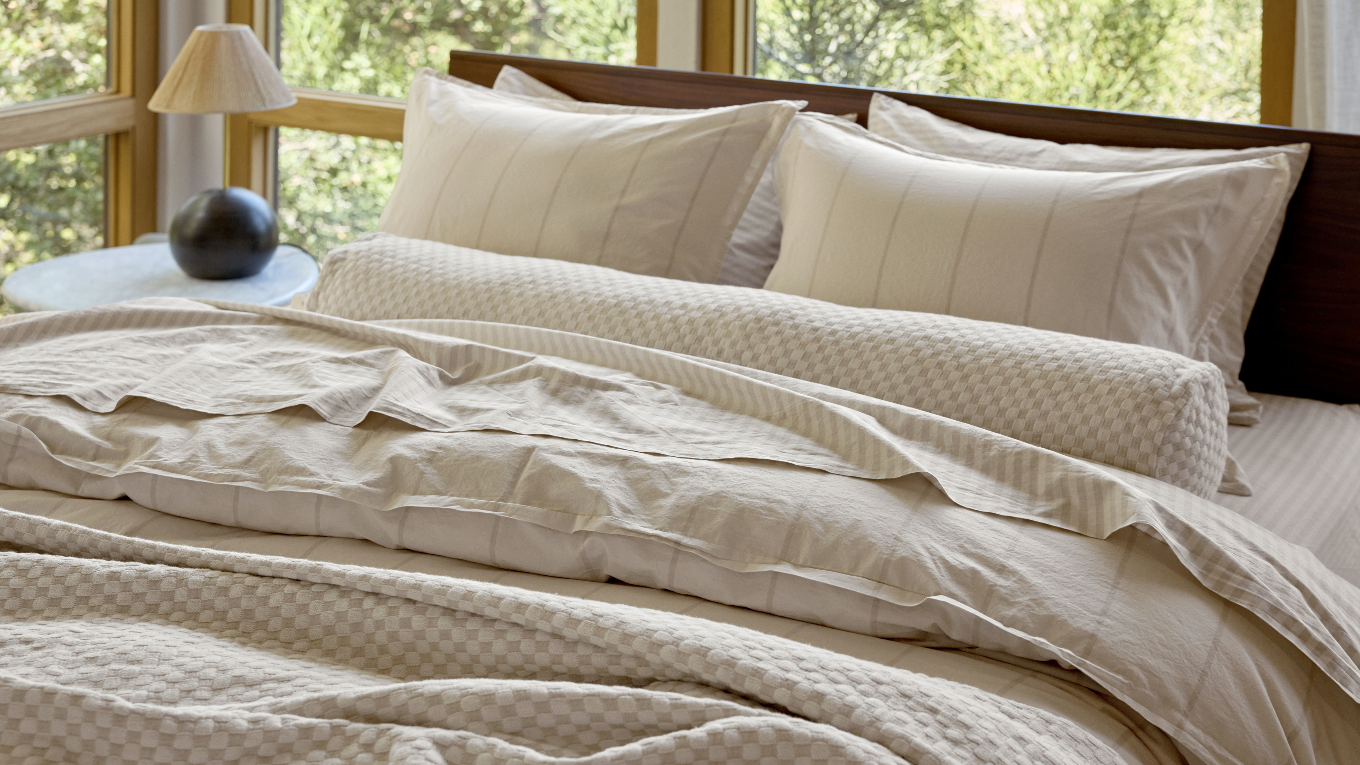 Beige Parachute yarn-dyed striped bedding photographed on a large bed surrrounded by large windows