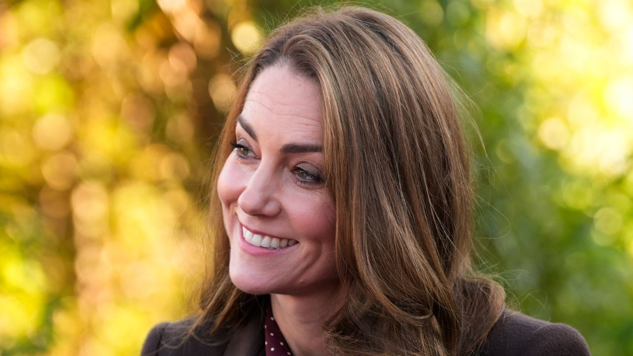 A headshot of Kate Middleton smiling in front of yellow and green trees