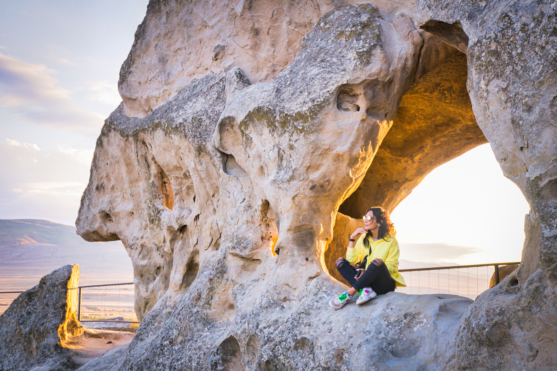 Woman sits on the rocky Uplistsikhe, Georgia structure and enjoys panoramic views