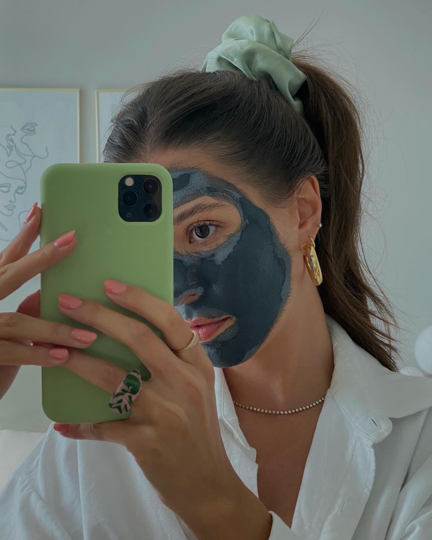 A woman taking a selfie wearing a clay face mask