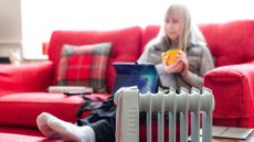 Winter Fuel Payment: older woman reading digital tablet with a cup of tea next to radiator 