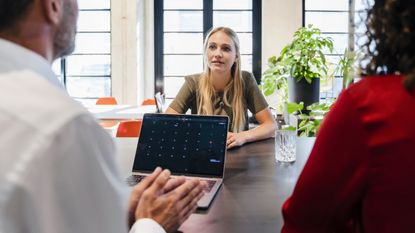 A young woman sits at a table for a job interview, facing a businessman and a businesswoman.