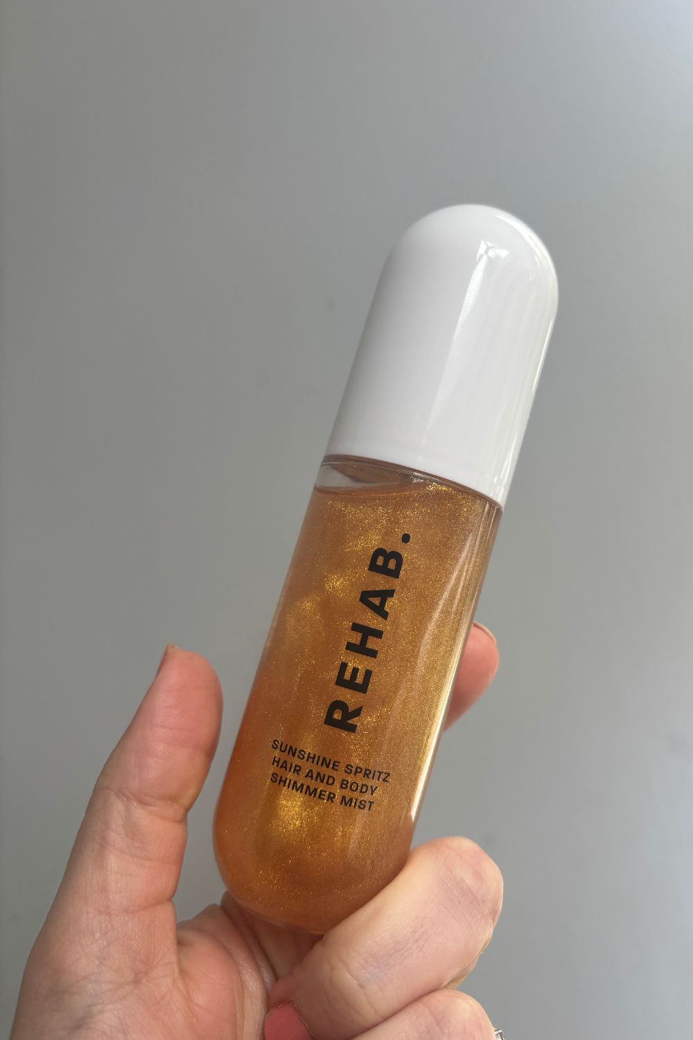 A hand holding a bottle of rehab sunshine spritz