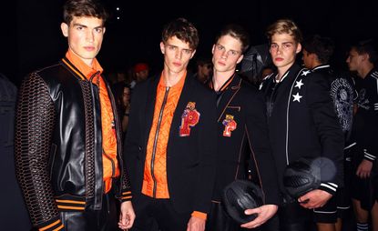 4 male models wearing dark clothing and posing for the camera in a crowded room