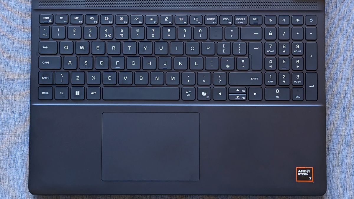 A laptop keyboard with a full numeric keypad sits above a centered touchpad, and an AMD Ryzen 7 sticker is visible on the lower right of the palm rest.