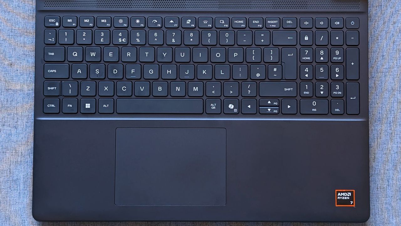 A laptop keyboard with a full numeric keypad sits above a centered touchpad, and an AMD Ryzen 7 sticker is visible on the lower right of the palm rest.