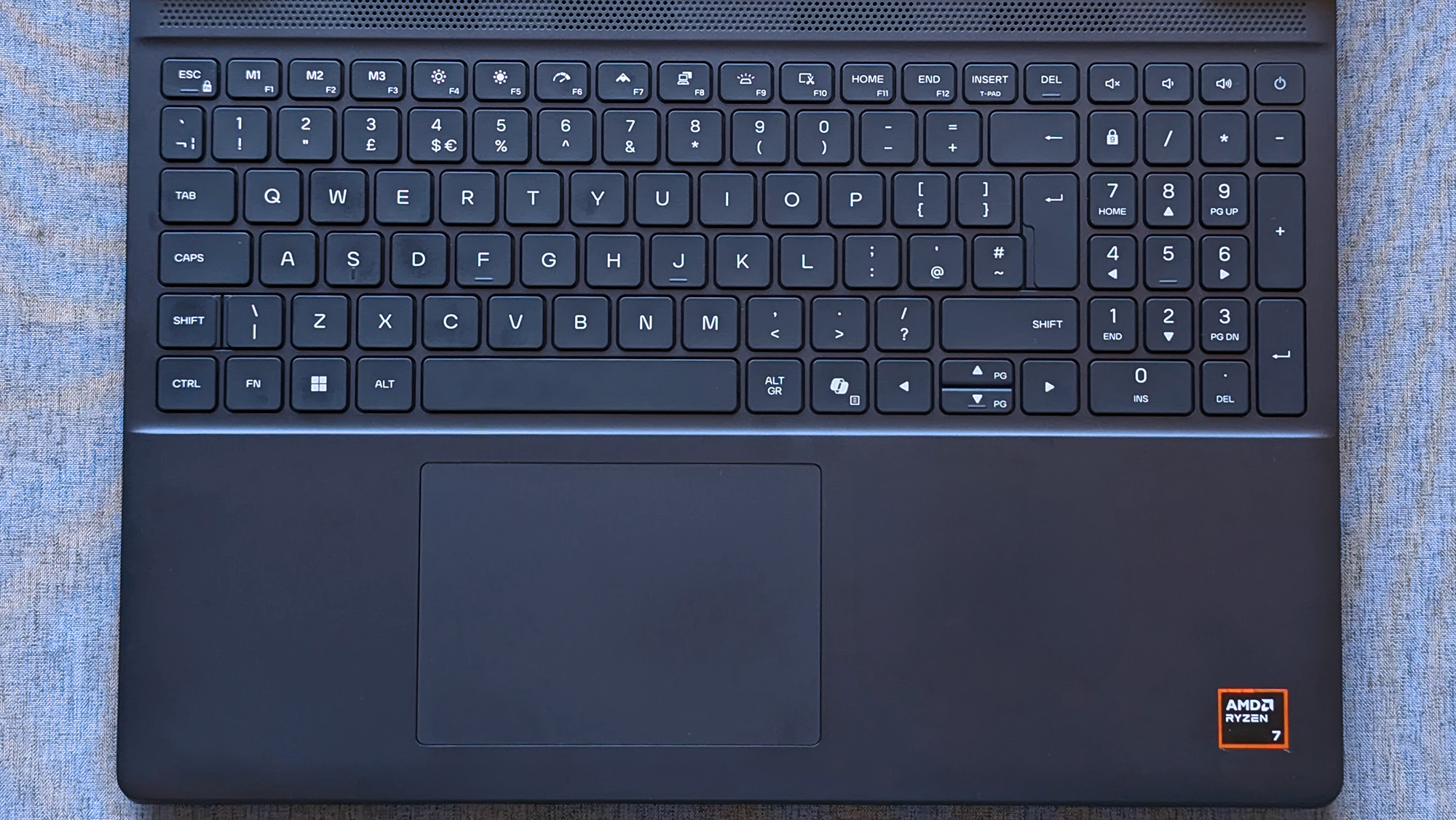 A laptop keyboard with a full numeric keypad sits above a centered touchpad, and an AMD Ryzen 7 sticker is visible on the lower right of the palm rest.