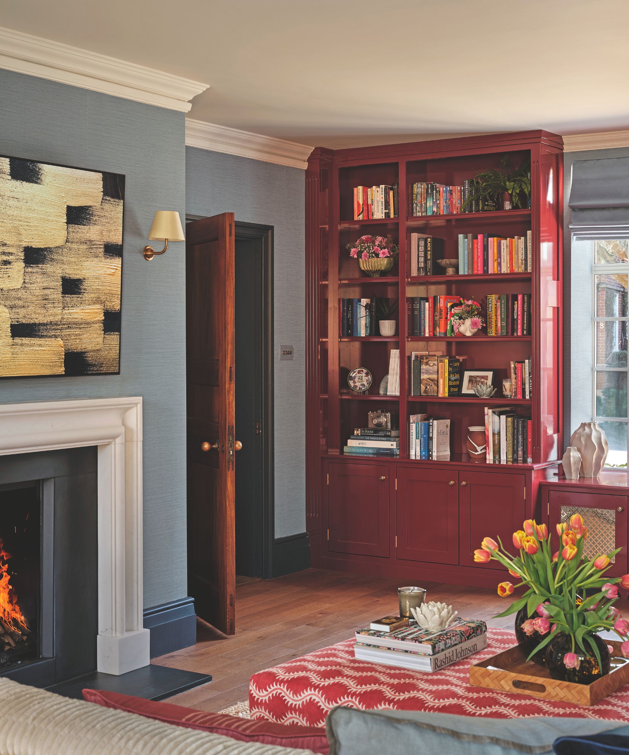 Inviting living room with a white fireplace, blue walls, red built-in bookshelves, and a coffee table topped with books and a tray of tulips