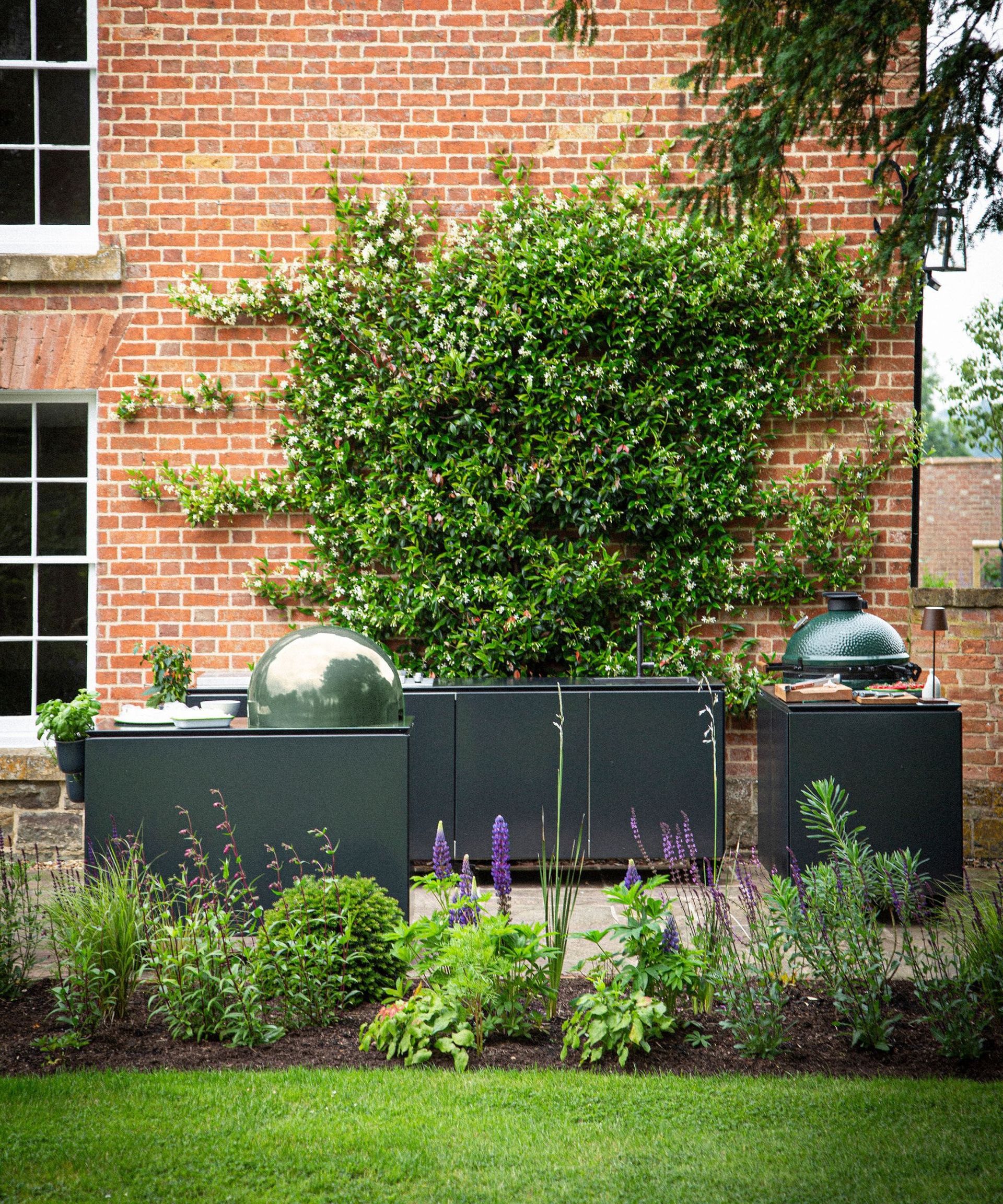 A dark gray outdoor kitchen next to a herbaceous border