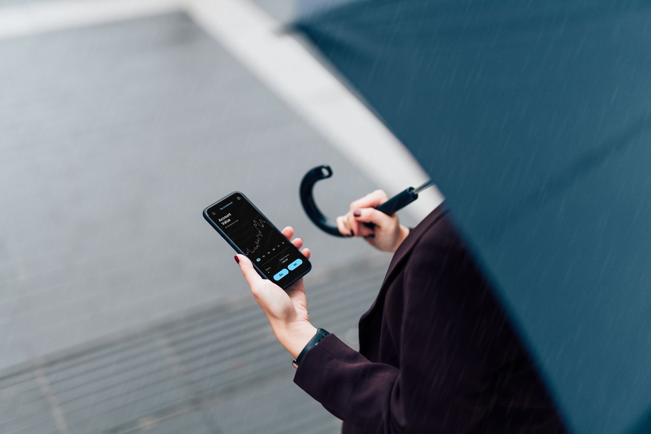 A woman checks her phone while holding an umbrella (image: Getty Images)