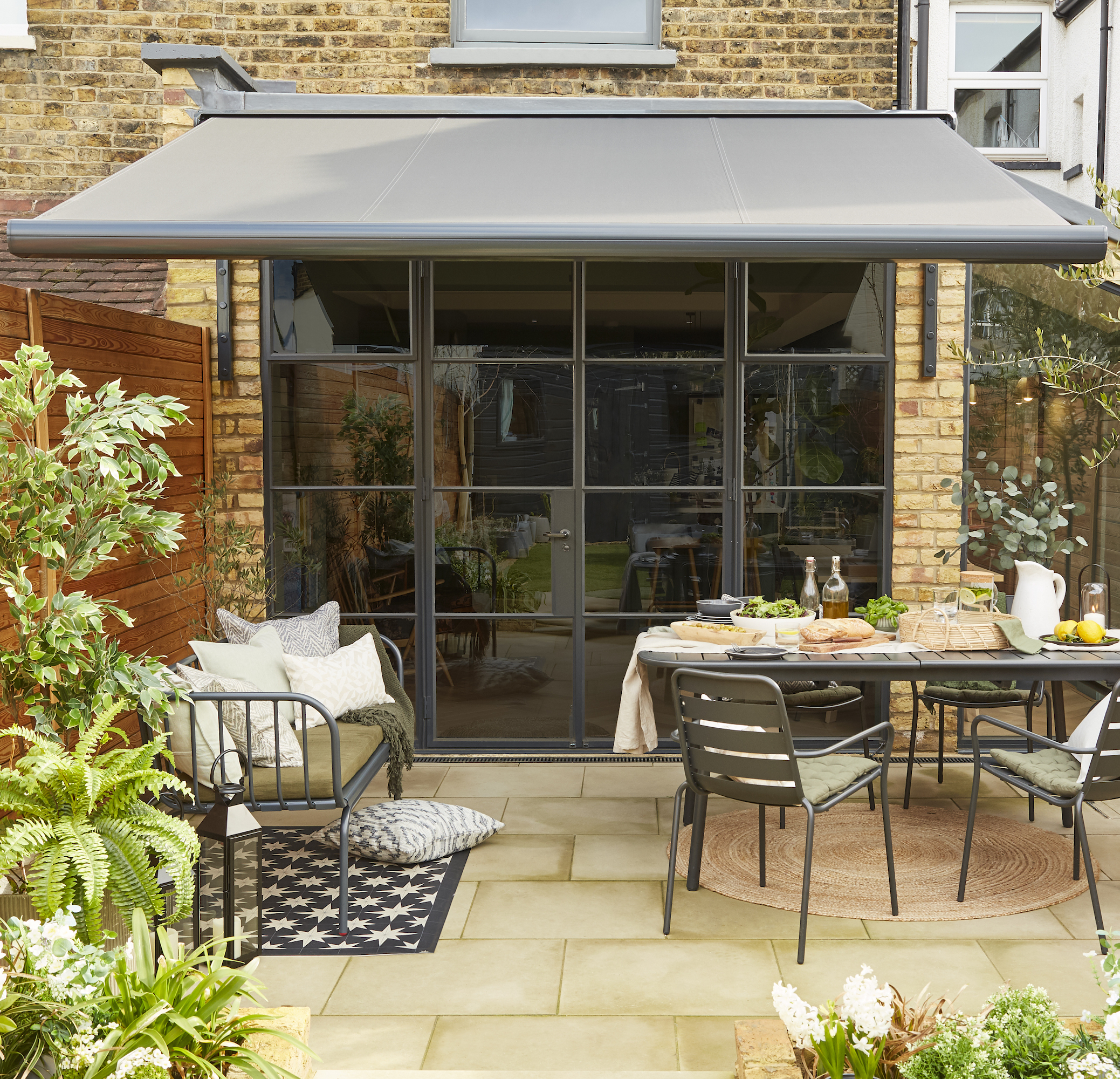 Awning above garden patio area with table, chairs and bench