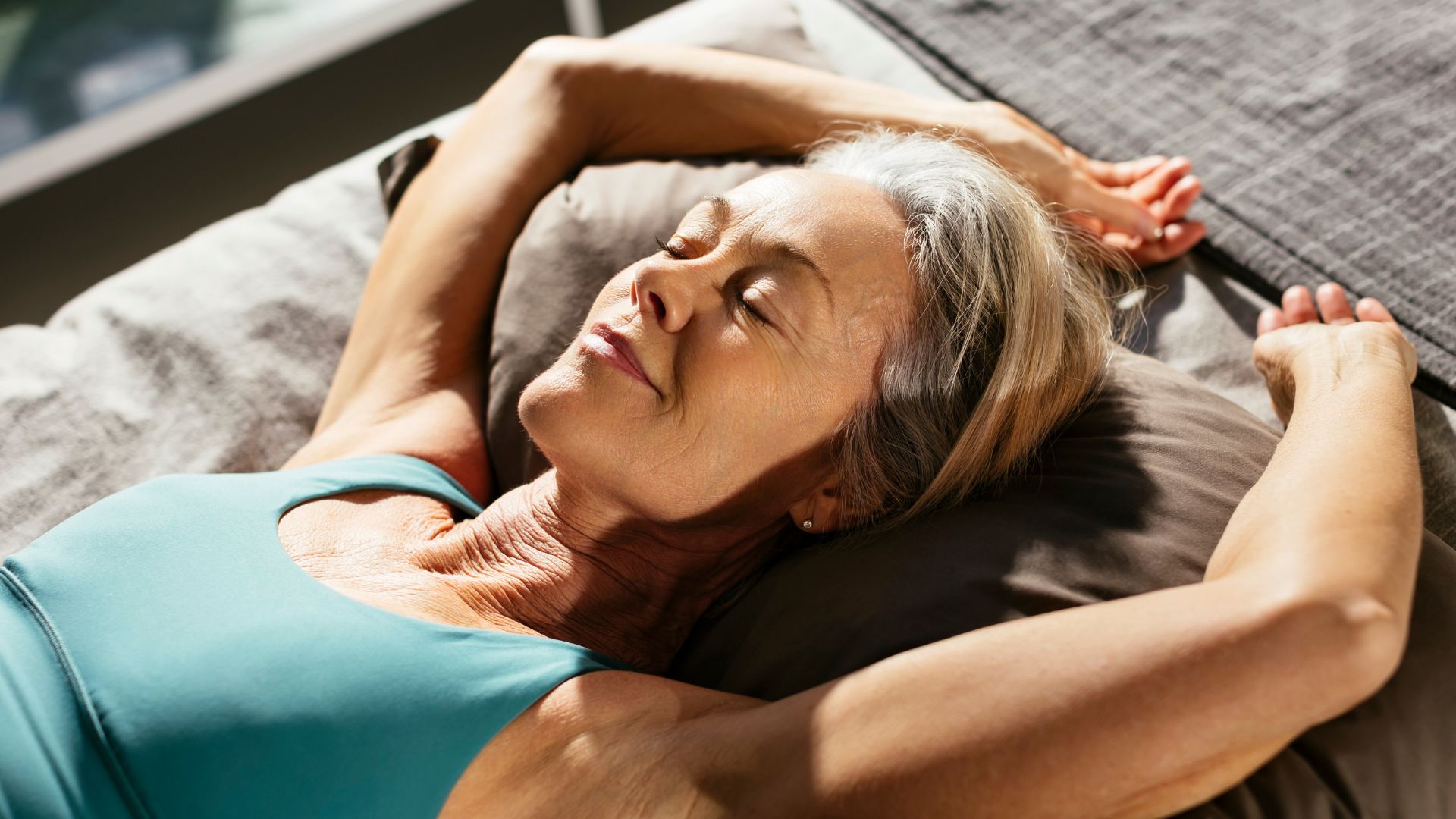 A woman lies on her back in bed with her arms above her head and her eyes closed.