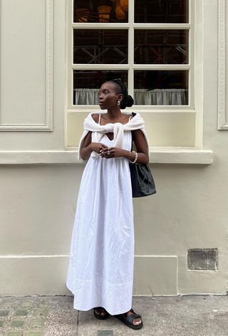 a photo of a woman's white dress outfit with a white maxi underneath a cream sweater styled with black sandals and a black tote