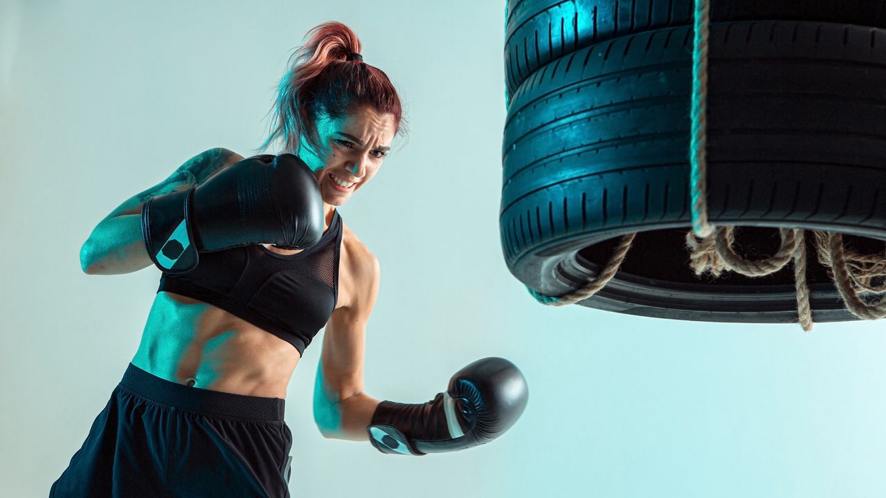 Best boxing gloves: pictured here, a fit young woman using boxing gloves to punch some suspended tyres in a photo studio