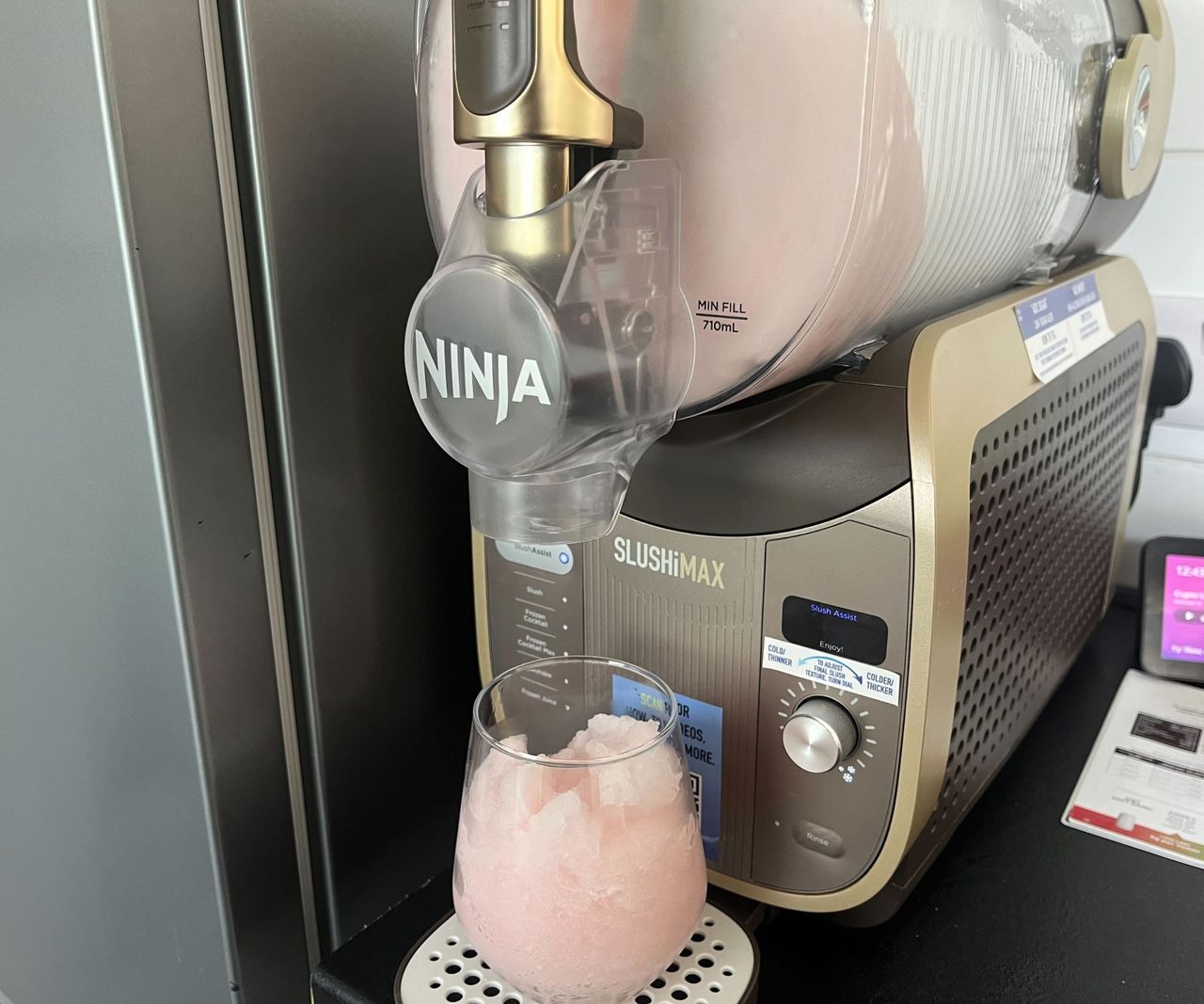 The Ninja SLUSHi max filled with pink slush, and a glass of pink slush on the drip tray.