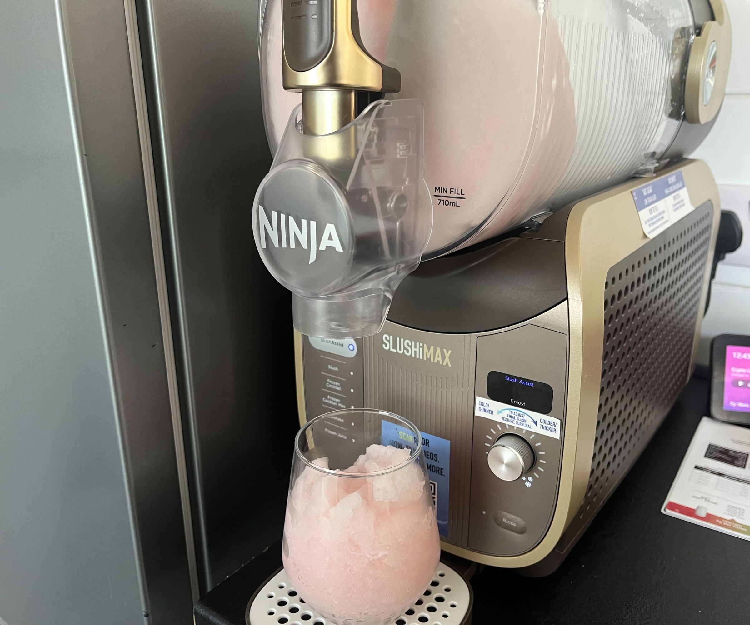 The Ninja SLUSHi max filled with pink slush, and a glass of pink slush on the drip tray. 