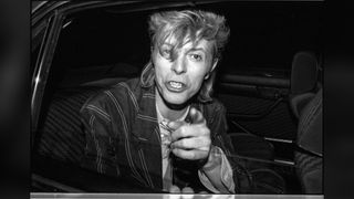 Black and white photo of David Bowie leaning out of a car window at night, pointing angrily at the camera with his teeth bared.