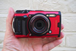 Et rødt og svart actionkamera av typen Olympus TG-6 holdt i en hånd.