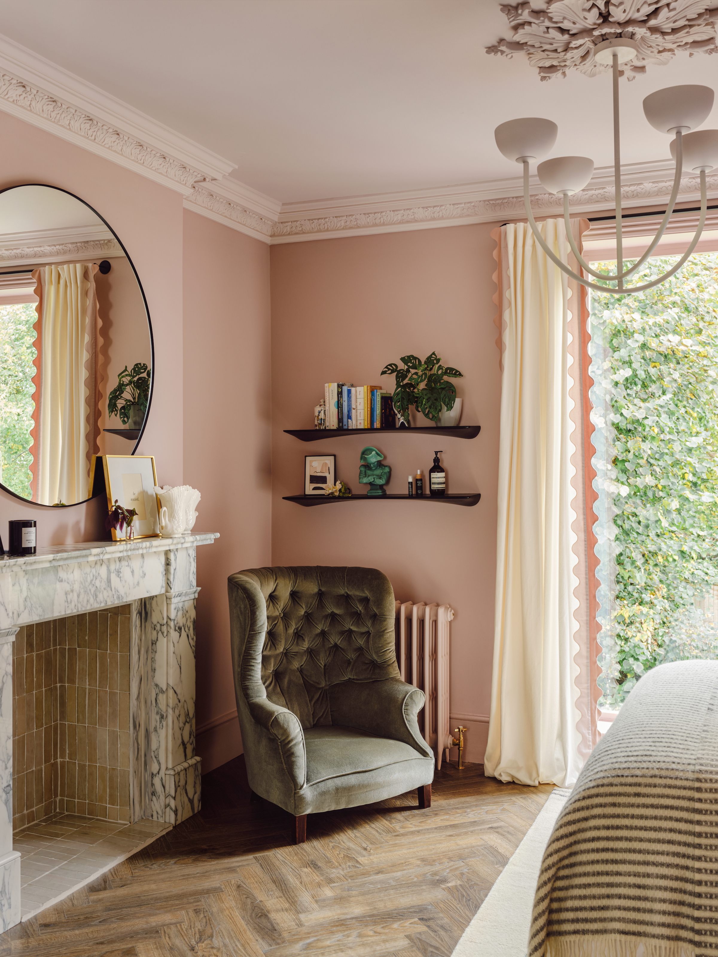 Pink bedroom with white and grey marble fireplace, green velvet armchair and black shelving