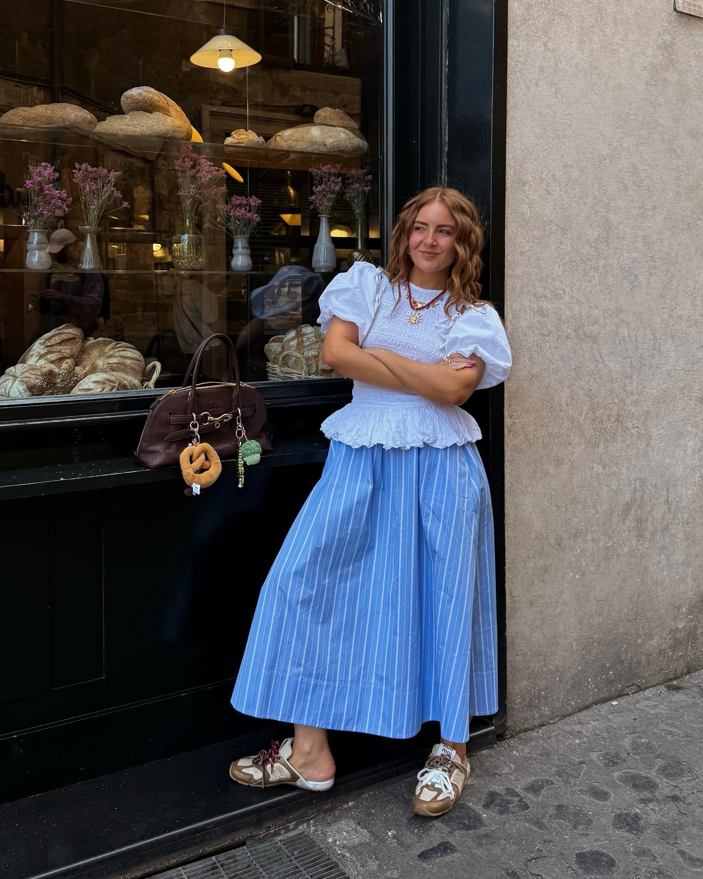 Influencer wears the Damon Madder white blouse with detachable sleeves with a blue striped skirt and mule trainers.