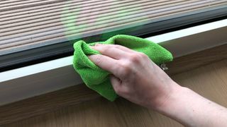 A microfiber cloth dusting the frame of a window