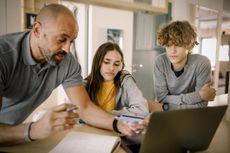 Brother and sister looking at father explaining finance with credit card at kitchen island