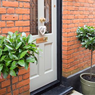 Front door of a red brick house with two potted bay trees