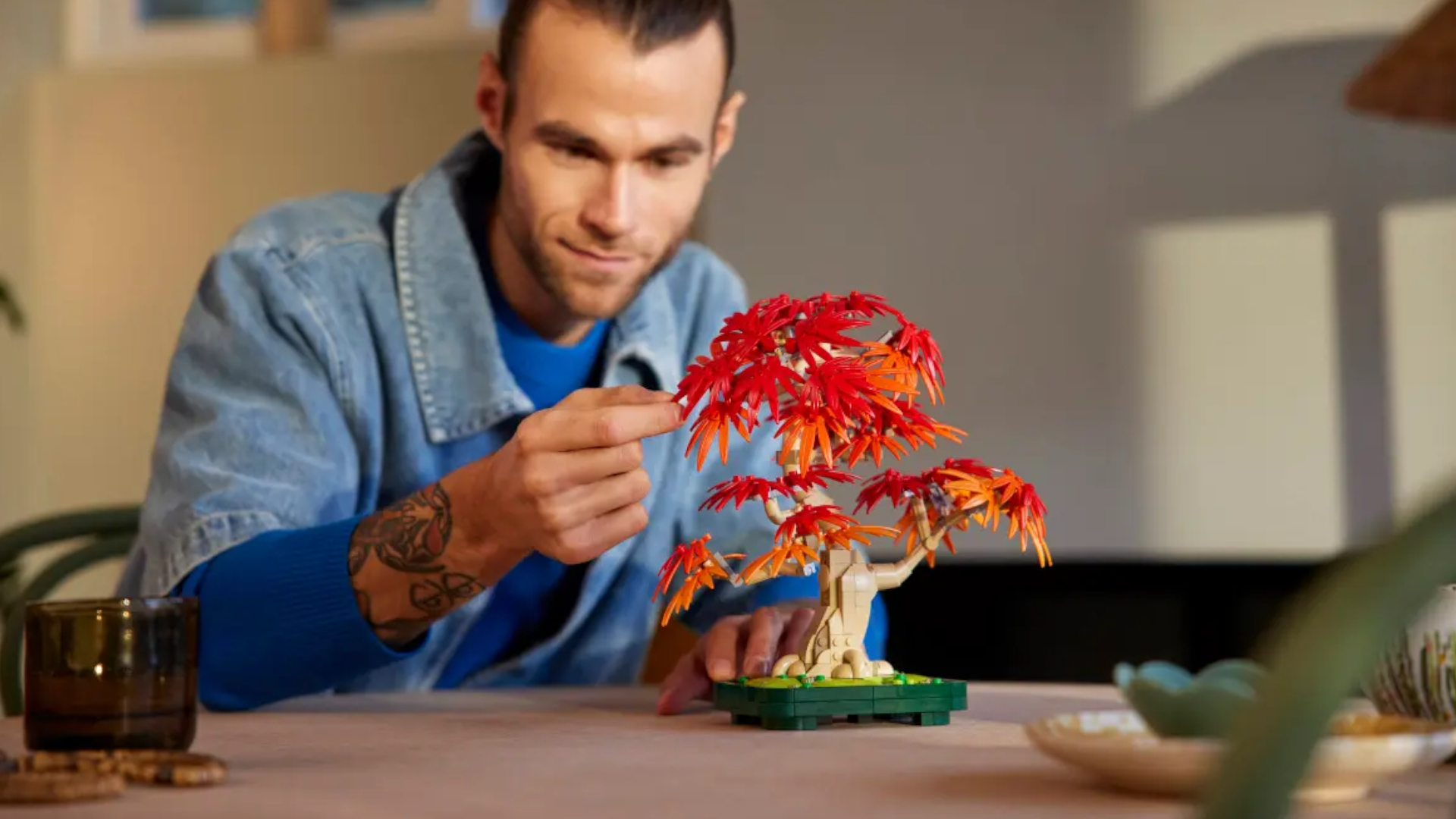 A smiling man puts the final piece on a Lego Japanese Red Maple Bonsai Tree set