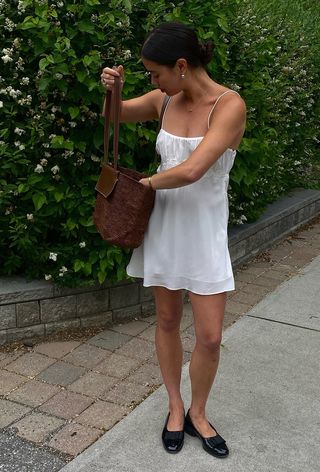 summer wardrobe essential shown on a woman wearing a woven tote bag with a white dress and black ballet flats