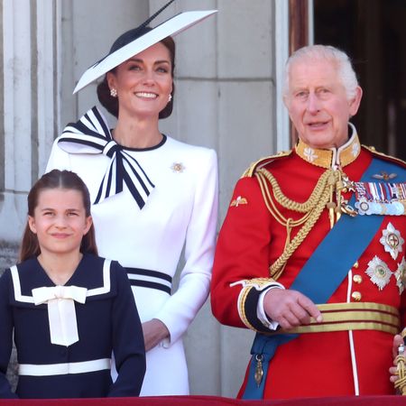 Princess Charlotte wears a navy dress with white accents, while mom Princess Kate wears a white dress with a navy bow, and King Charles wears red military uniform