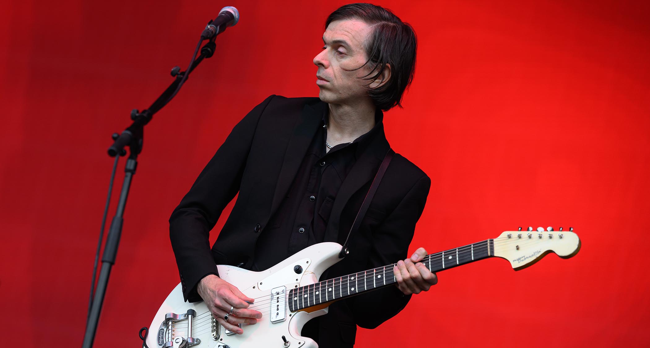 Barrie Cadogan plays a custom Fender offset against a stage backdrop of deep red