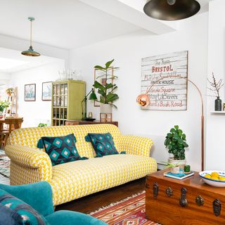 living room with white wall and yellow sofa with cushions and vintage trunk