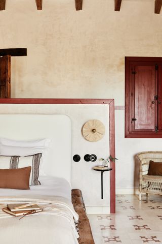 A rustic bedroom with geometric red patterned tiles, a headboard with red accents and red shutters