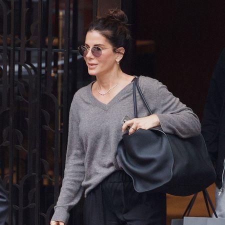 Sandra Bullock wearing a gray V-neck sweater, black pants, and mesh flats