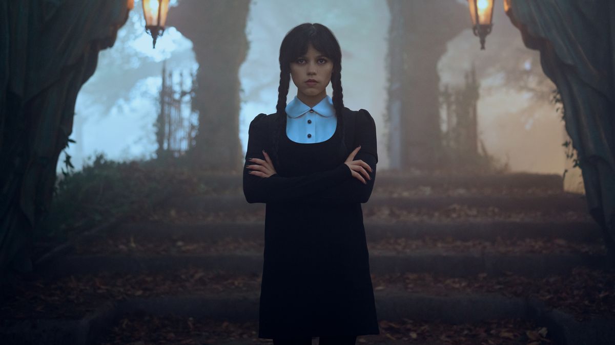 Wednesday crosses her arms in front of an eerie staircase in Wednesday season 2