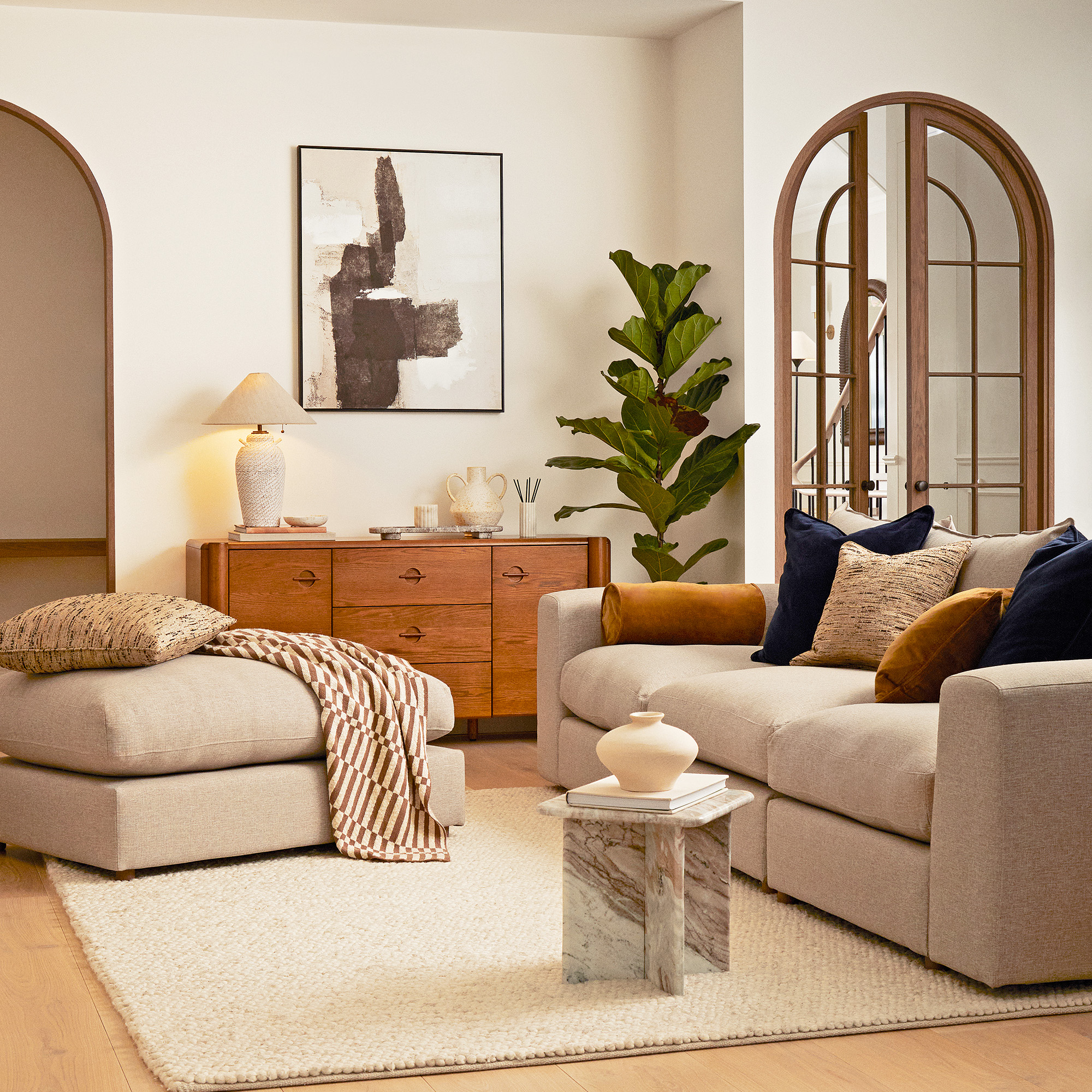 cream living room with beige sofa and footstool with wooden sideboard and textured cream rug on wooden floor