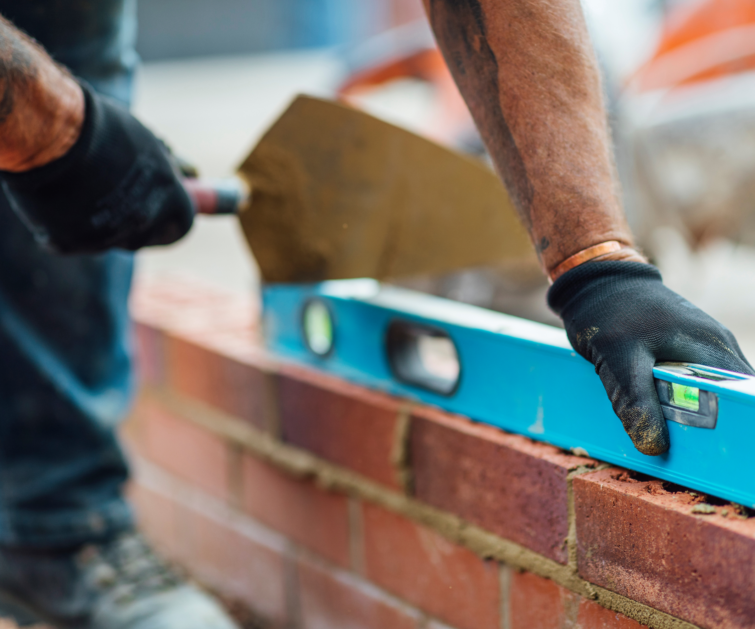 close up of hands laying a brick wall using a blue spirit level and trowel