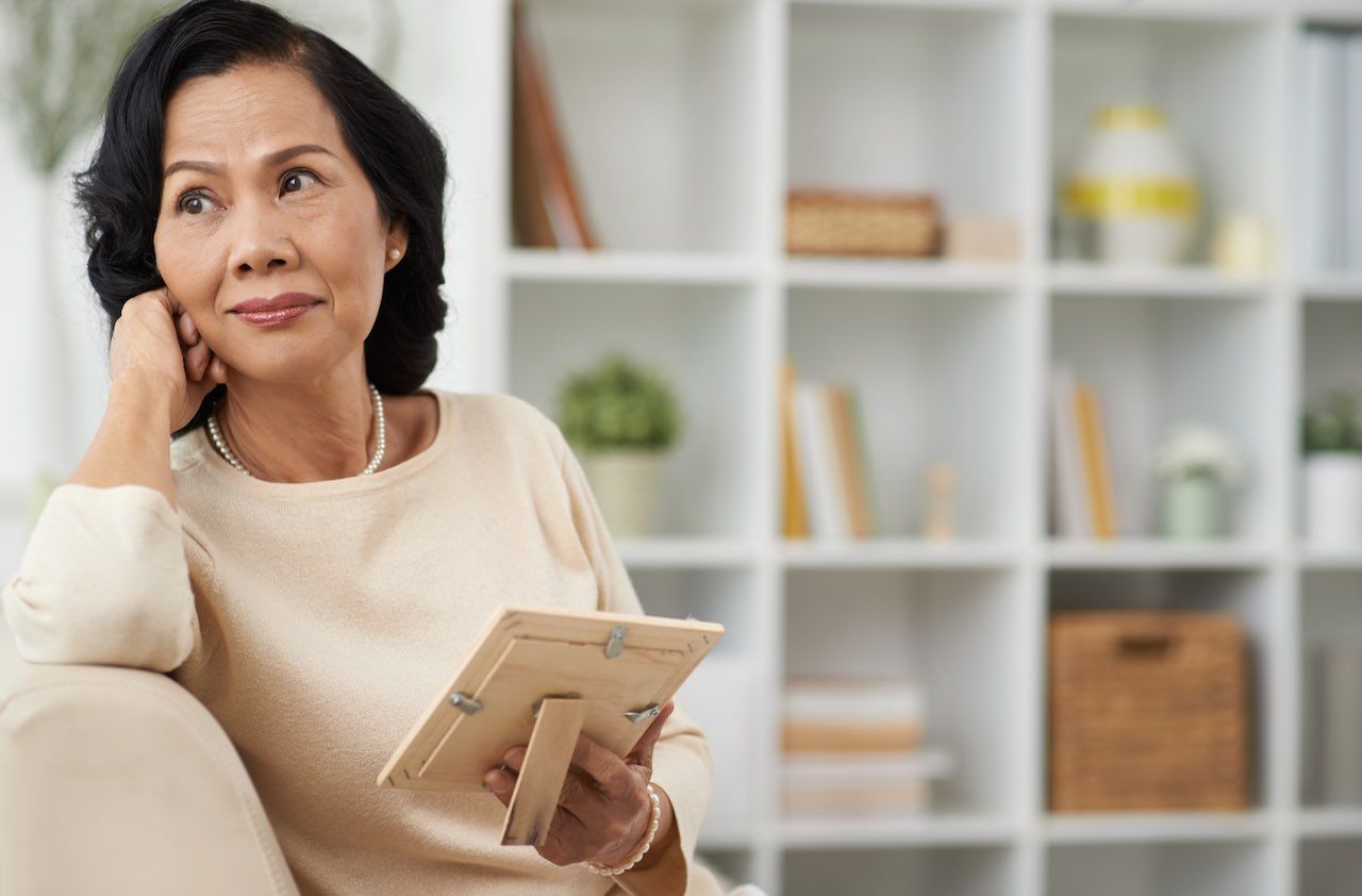 Pretty mature woman with a photo in her hands looking thoughtfully to the side