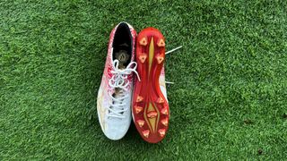 Red and white football boots side by side with one upside down on green artificial grass.