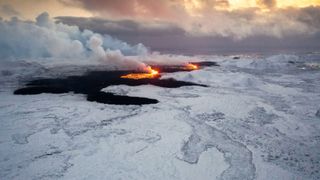A drone is capturing the lava flow from the erupting volcano on the Reykjanes Peninsula, with the town of Grindavik and the lights of the famous Blue Lagoon visible in the background, in Grindavik, Iceland, on December 19, 2023.