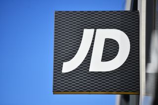 JD Sports logo on a square sign fixed to one of its high street stores, with a clear blue sky in the background