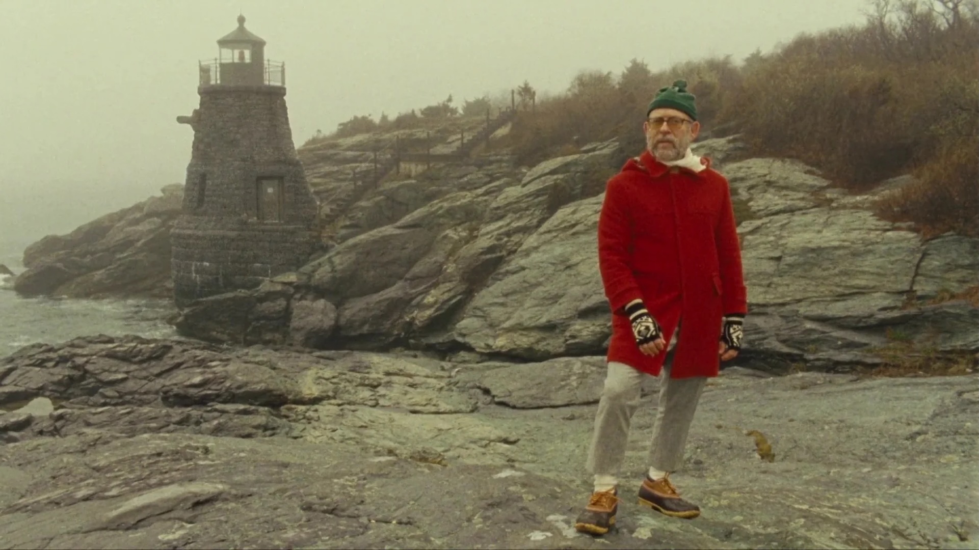 The Narrator from the film Moonrise Kingdom, standing in front of a lighthouse.