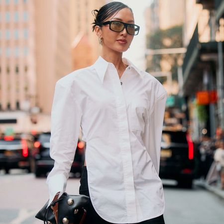 Woman is wearing a white button down top and black skirt while holding a handbag with lots of accessories. She is also wearing sunglasses. 