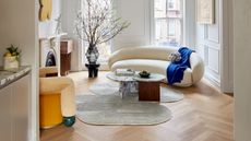 a living room with an irregularly shaped rug, yellow wall art and accent chair, and a curved white sofa