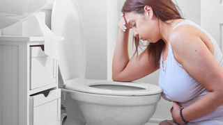 Woman knelt at the toilet with her head in her hands looking like she is going to be sick