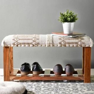 A shoe storage bench with shoes underneath and a cushioned top with a plant on it